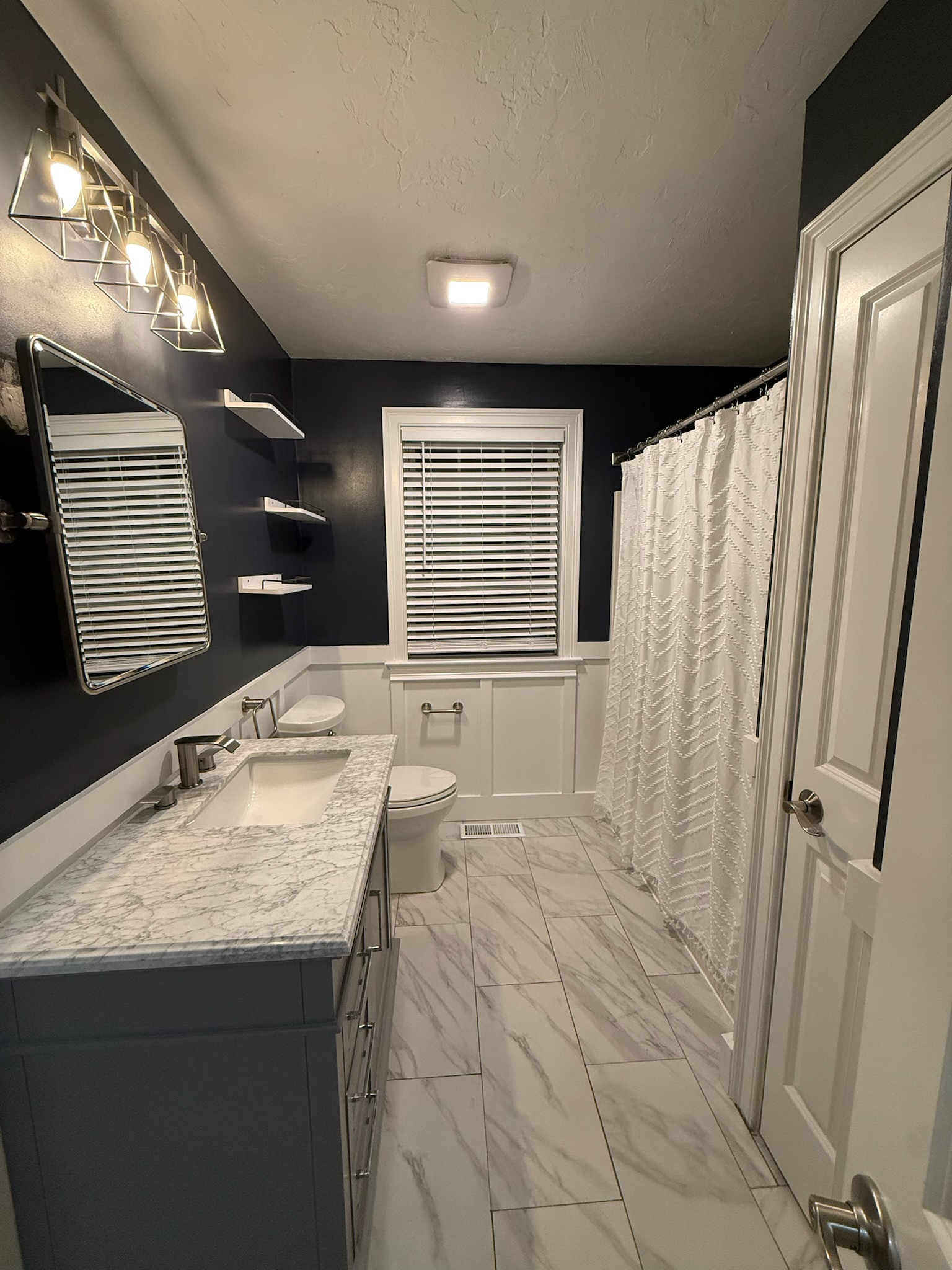 Tewksbury bathroom renovation — navy walls with white wainscoting and marble tile